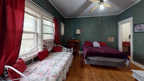Classic bedroom with two beds, a desk, and a ceiling fan, set against a floral wallpaper backdrop.