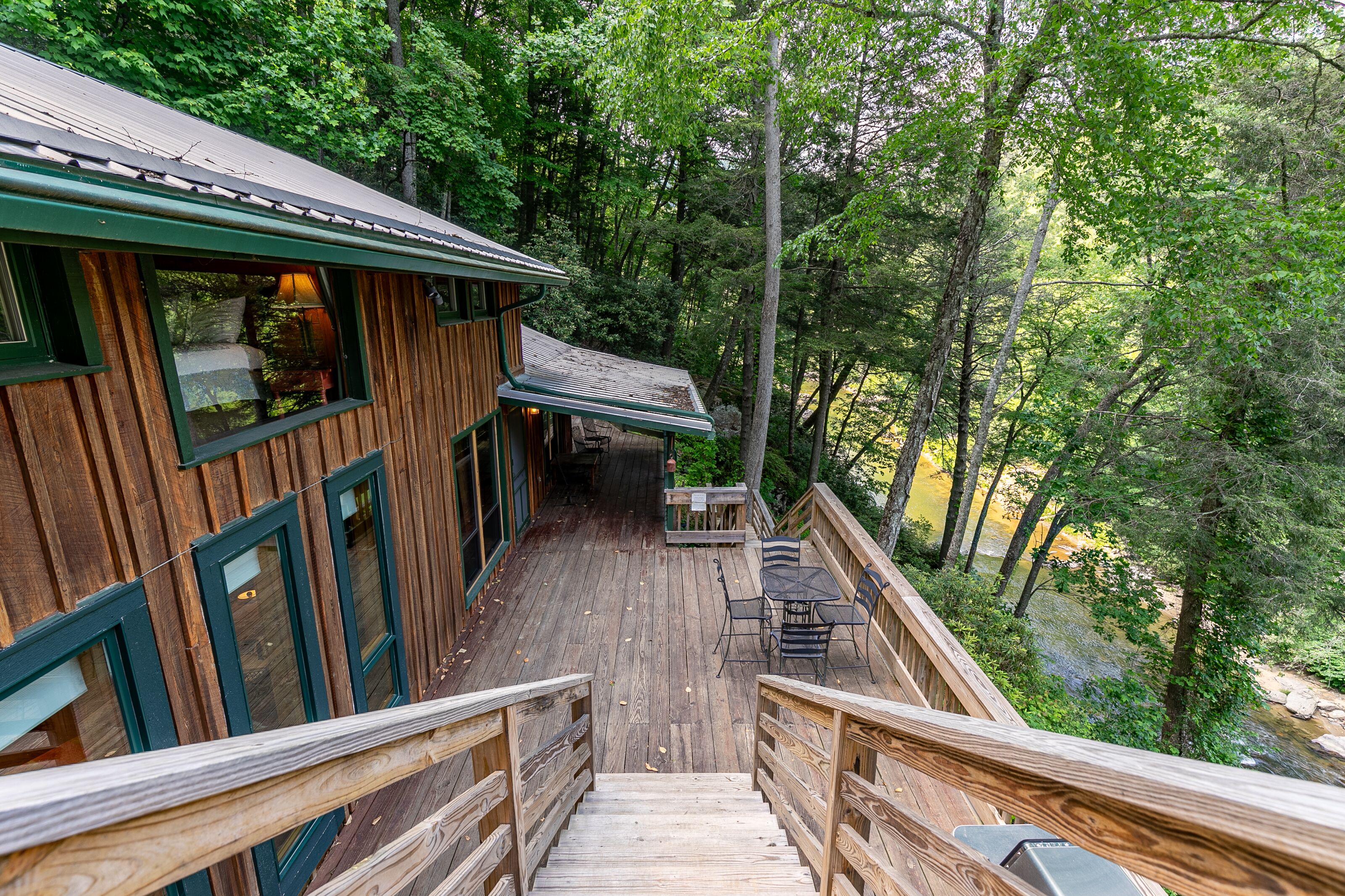 A wooden deck with a staircase leading to a cabin surrounded by dense forest.