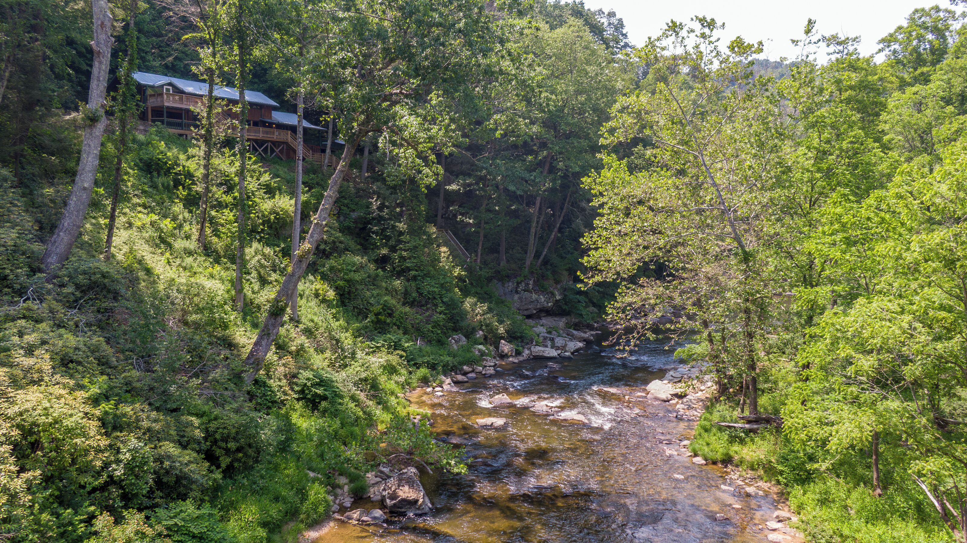 A cabin with a deck overlooking a forested area and a stream.