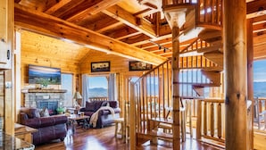 A wooden cabin interior with a fireplace, wooden staircase, and a cozy living area with a couch and coffee table. - 100-Mile Views: 3 King Suites I Hot Tub I Game Rm-Pool Table/Arcade/Air Hockey (Sevierville)