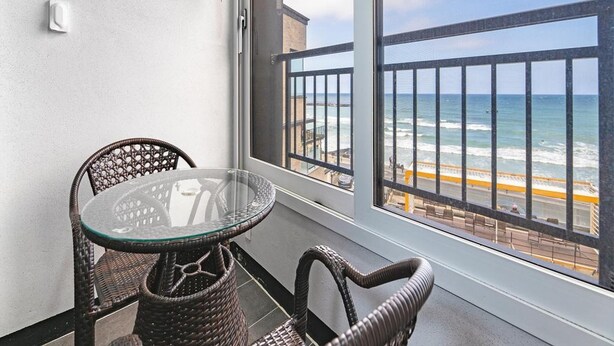 Un balcón con mobiliario de mimbre, una mesa de vidrio y vista a la playa y al océano.