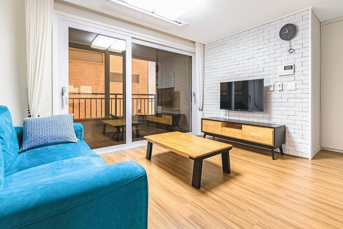 A modern living room with a blue sofa, a wooden coffee table, and a TV mounted on a white brick wall.