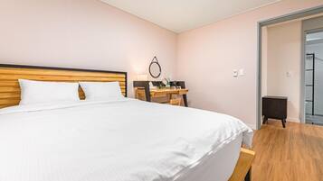 Habitación de hotel ordenada con una cama grande, un escritorio de madera y una pequeña silla.