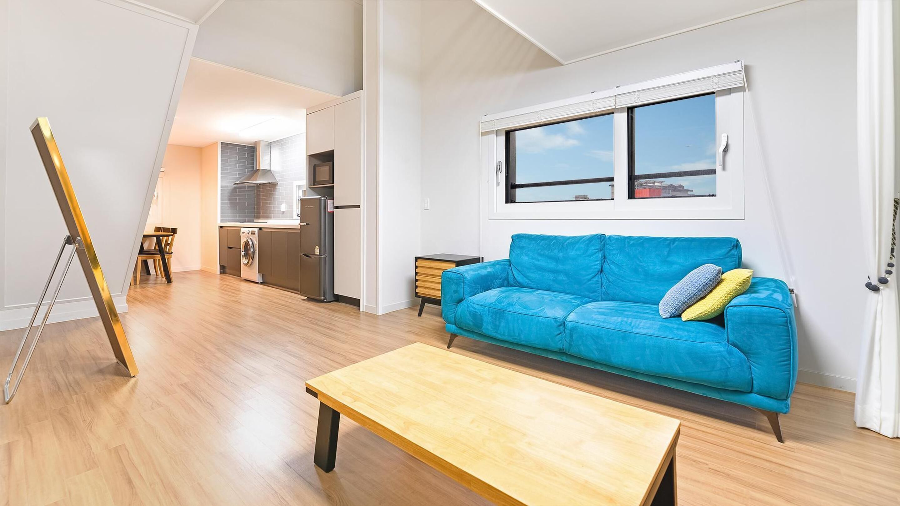 A spacious living area with a blue sofa, wooden coffee table, and a kitchen in the background.