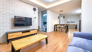 Una sala de estar moderna con un televisor montado en una pared de ladrillo, un banco de madera, un sofá azul y un comedor con mesa y sillas.