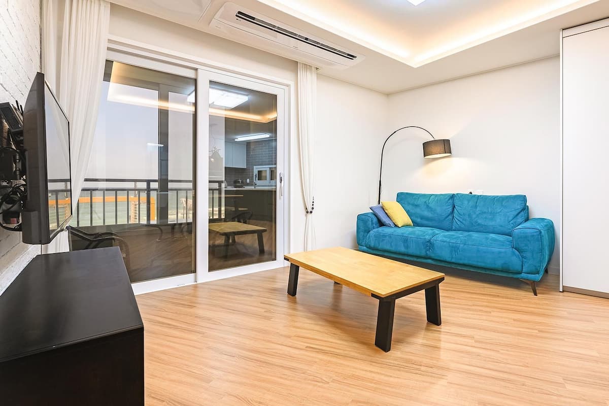 A modern living room with a blue sofa, a wooden coffee table, and a TV on a black stand.