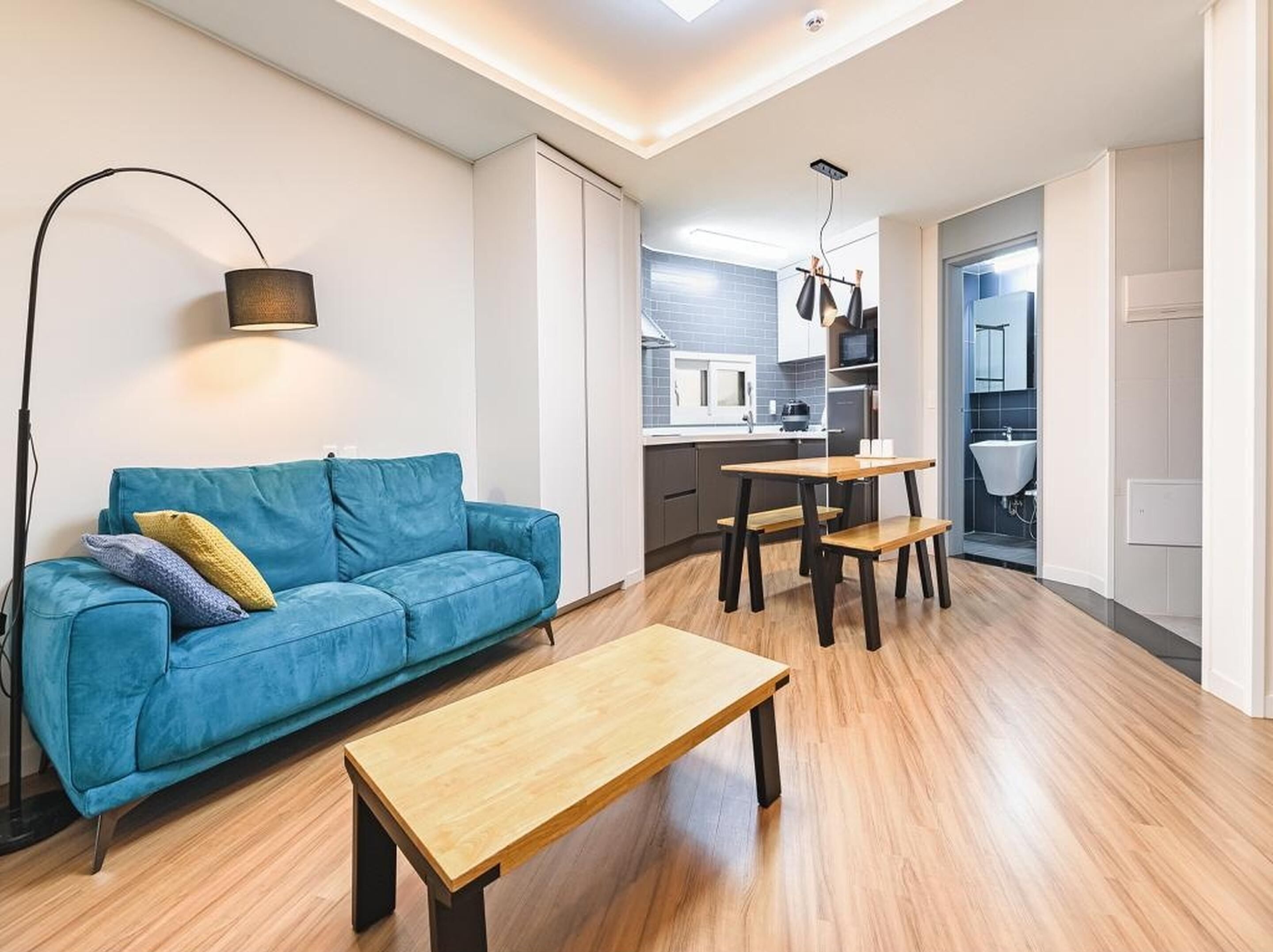A modern living room with a blue sofa, a wooden coffee table, and a dining area with a small table and benches.