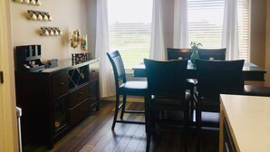 Un coin repas avec une table et des chaises, un espace dédié au café avec des tasses, et une vue par la fenêtre.