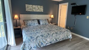 Een slaapkamer met een bed, twee bedlampen, een aan de muur bevestigde televisie en een deur.