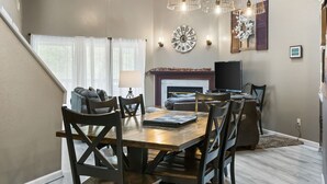 Un comedor con una mesa y sillas de madera, una chimenea, un televisor y un reloj en la pared.