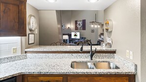 Una cocina con encimeras de granito, pileta de acero inoxidable, armarios de madera y un reloj de pared decorativo.