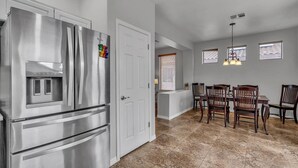 A modern kitchen with a stainless steel refrigerator, a dining area with wooden chairs, and a kitchen island. - Dive Into Spring in Mesa | Community Pool, Hot Tub, Tennis & Hoops (Mesa)