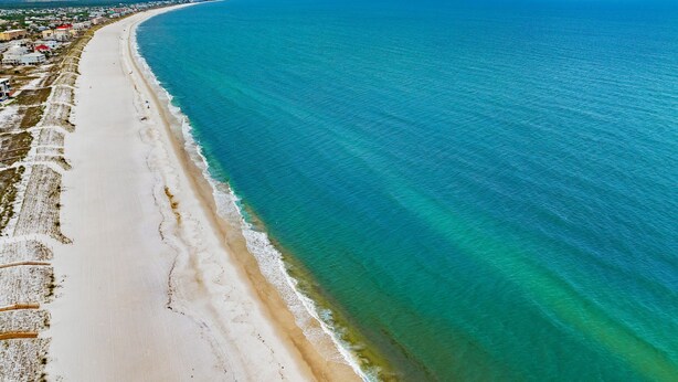 Vista aérea de uma área costeira com uma extensa praia de areia e mar azul cristalino.
