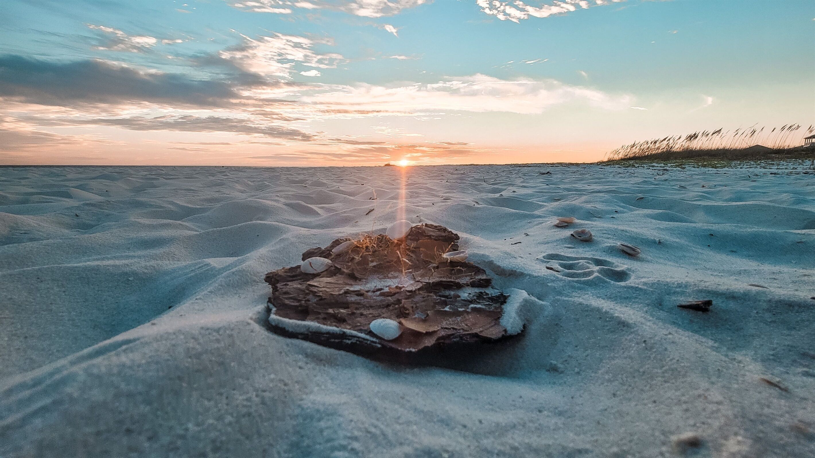 A sandy beach with a rock formation in the center and a sunset in the background.