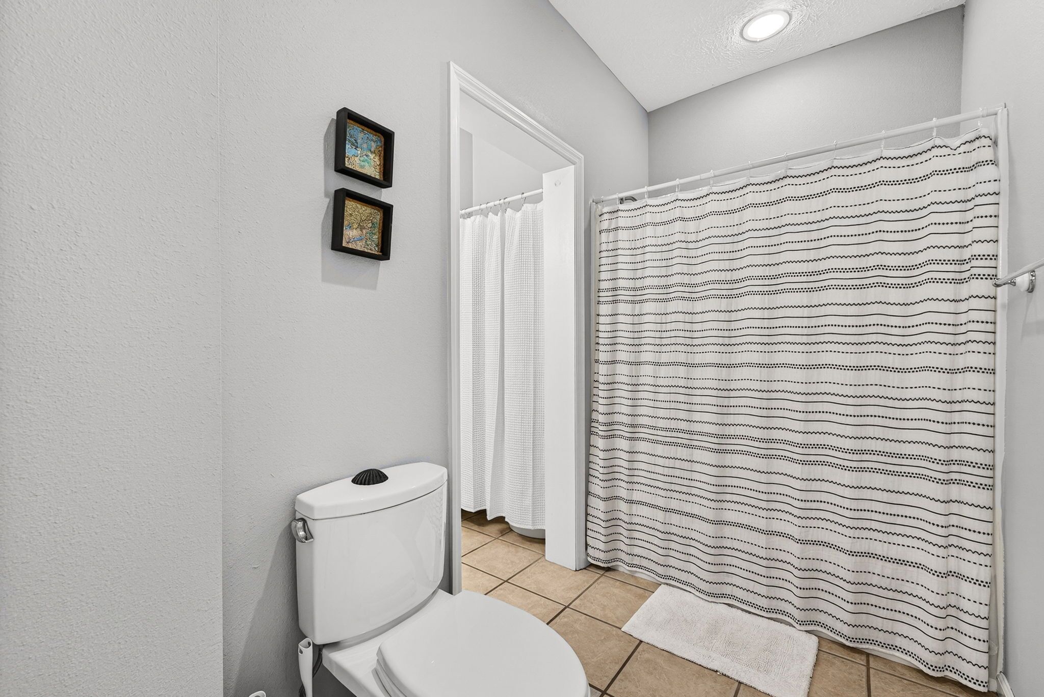 A bathroom with a toilet, a shower curtain, and two framed pictures on the wall.