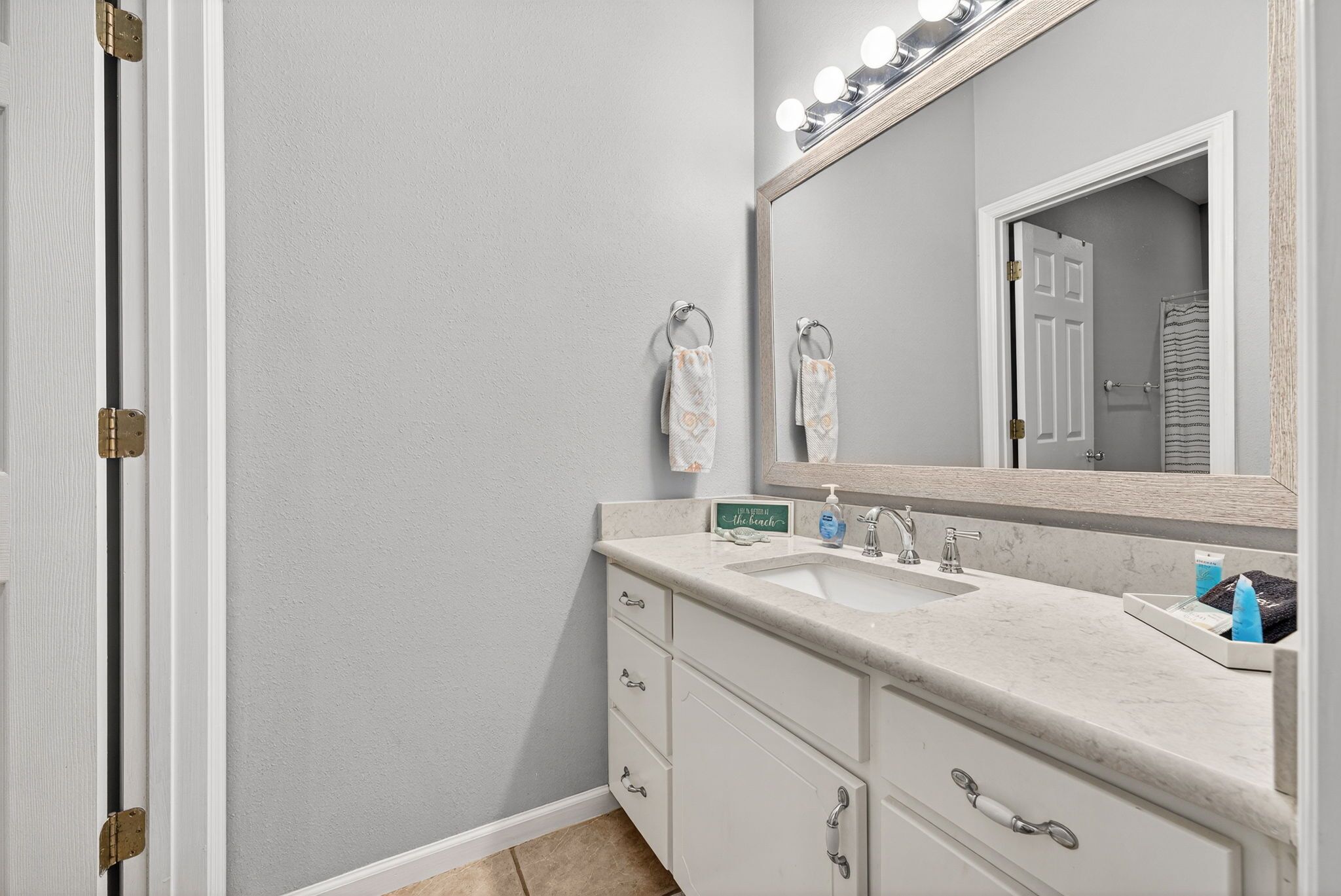 A bathroom with a double sink, vanity with drawers, a mirror with lights, and a towel rack.