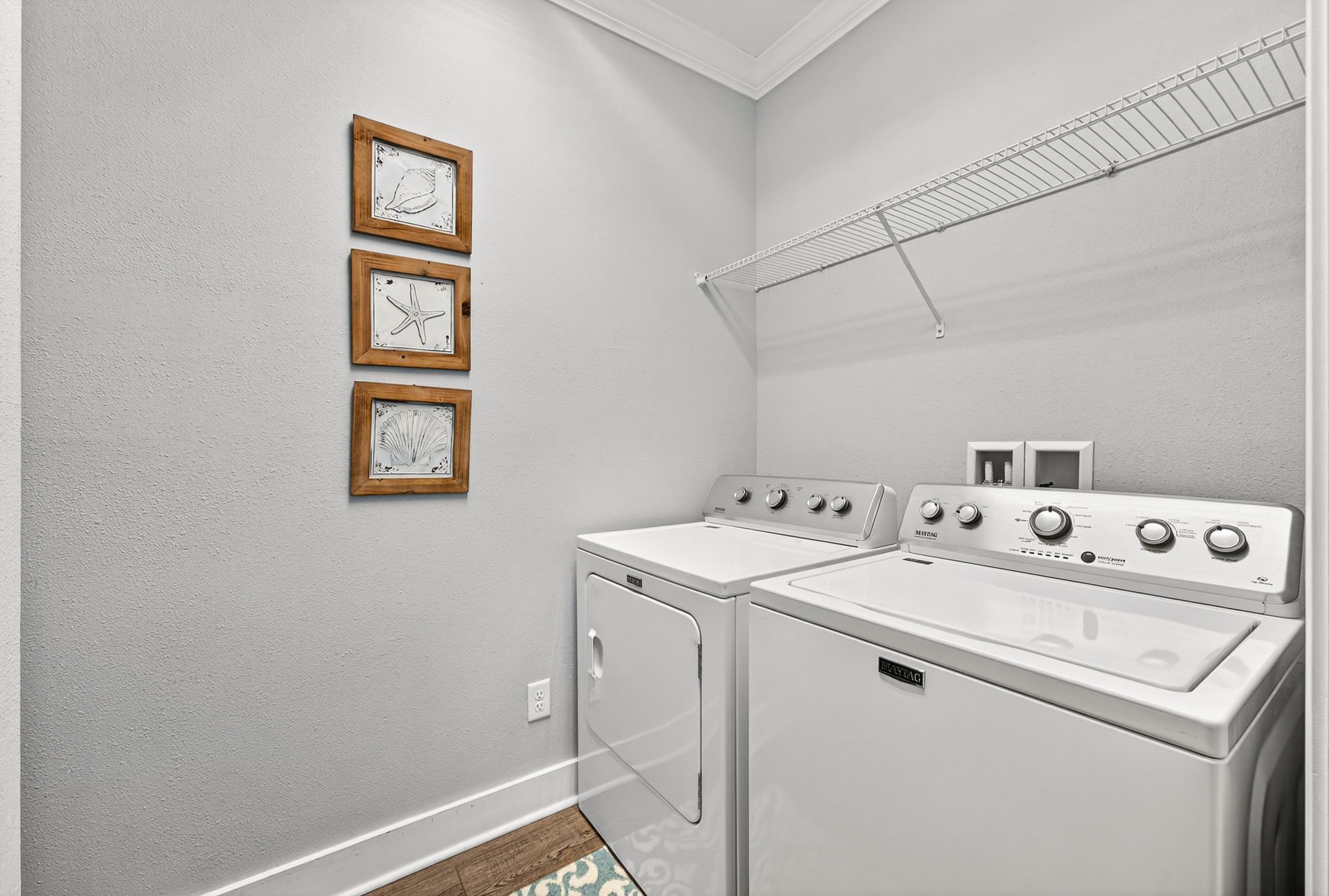Une buanderie avec deux machines à laver blanches, un étendoir et trois tableaux encadrés accrochés au mur.