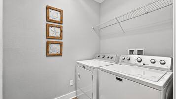 Une buanderie avec deux machines à laver blanches, un étendoir et trois tableaux encadrés accrochés au mur.