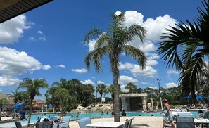 Zona de piscina con palmeras, sillas de descanso y un elemento acuático.