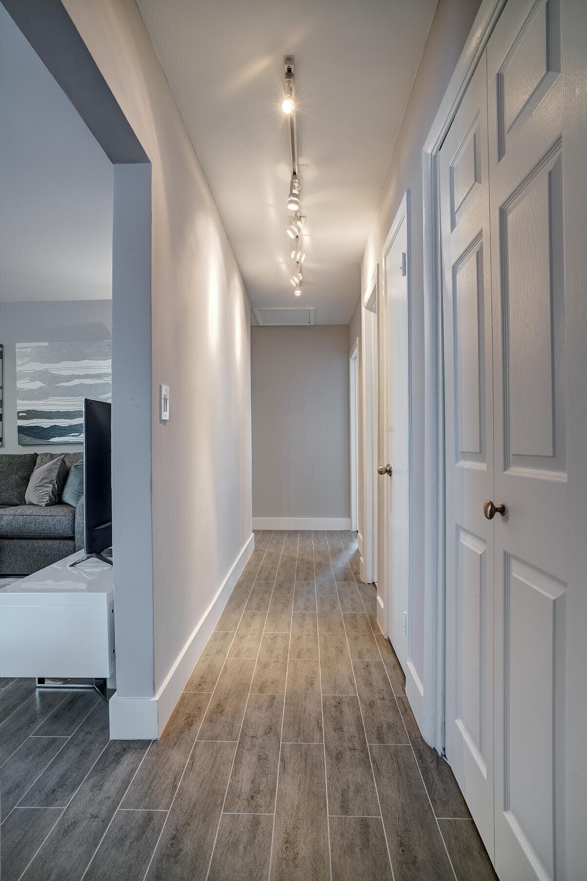 A hallway with a grey tiled floor, white walls, and a ceiling light fixture.