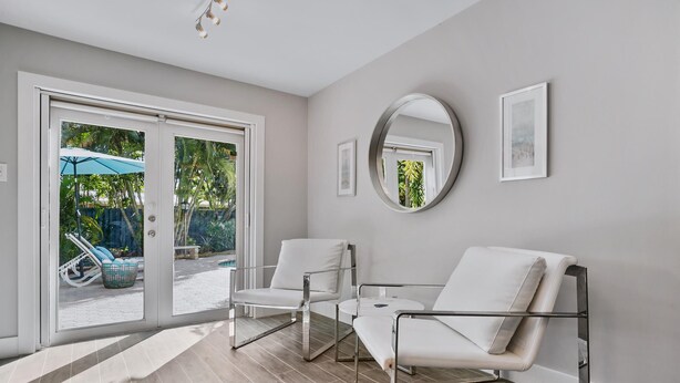 Une chambre moderne dotée d’une porte-fenêtre coulissante donnant sur un espace extérieur, d’un miroir rond accroché au mur et de deux chaises blanches.