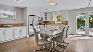 Une cuisine moderne avec des meubles blancs, des appareils en acier inoxydable et un coin repas comprenant une table et des chaises en verre.