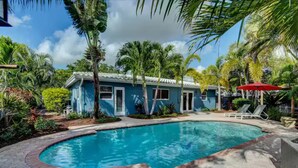 Un espace piscine avec une maison bleue, des palmiers et des chaises longues.