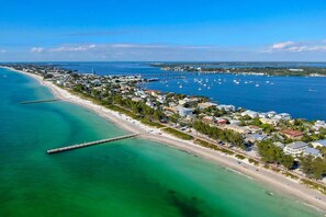 An aerial view of a coastal town with a beach, marina, and residential buildings.