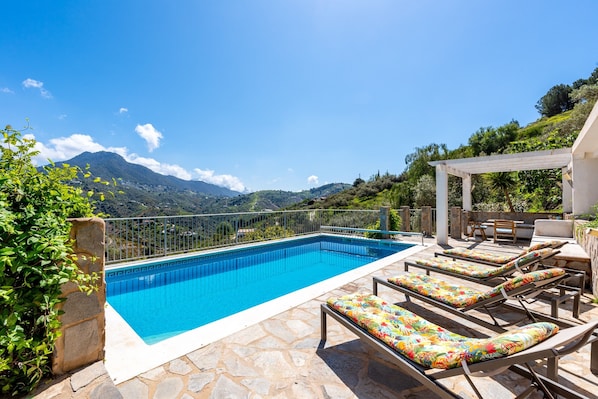 Une piscine avec des chaises longues, une pergola et une vue sur les montagnes.