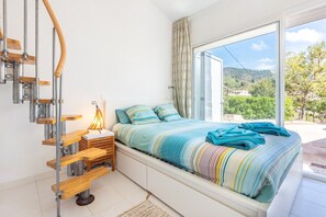 Une chambre à coucher avec un lit, un banc en bois, une lampe et une vue sur l’extérieur.