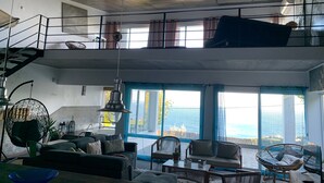 A spacious living area with a high ceiling, a balcony, and large windows offering a view of the sea. - Pet-Friendly Villa Azores SunriseHouse with Sea View, Pool, Jacuzzi, Wi-Fi, Terrace & Garden (Pedreira)