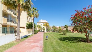 A pathway leading to a building with balconies, surrounded by palm trees and a well-maintained lawn. - Penthouse with a fantastic view, Mountain View, Sea View, Terrace & Garden (La Cala de Mijas)