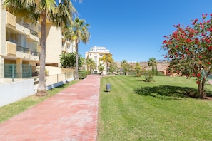 A pathway leading to a building with balconies, surrounded by palm trees and a well-maintained lawn. - Penthouse with a fantastic view, Mountain View, Sea View, Terrace & Garden (La Cala de Mijas)