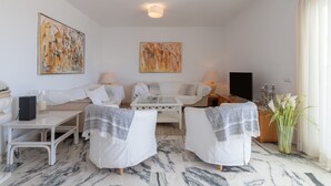 A modern living room with a sofa, armchairs, a coffee table, and two lamps. There are abstract paintings on the walls and a vase with flowers on the floor. - Penthouse with a fantastic view, Mountain View, Sea View, Terrace & Garden (La Cala de Mijas)