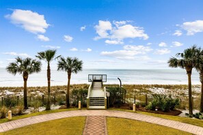 A beachside view with a pathway leading to a lifeguard tower, palm trees, and a sandy beach.