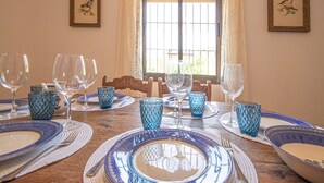 Une table à manger dressée avec de l’argenterie bleue et blanche, des verres et des couverts, avec une fenêtre et des tableaux encadrés accrochés aux murs.