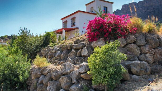 Un bâtiment blanc avec un toit rouge, entouré de rochers et de verdure.