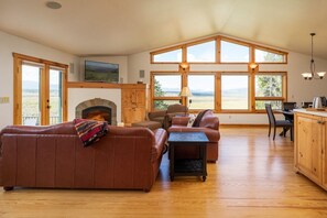 Un salón amplio con chimenea, sofás de cuero, una zona de comedor y ventanas grandes que ofrecen vistas al exterior.