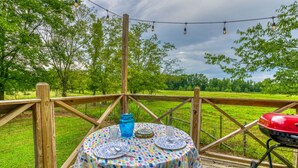 Une terrasse extérieure avec une table dressée pour les repas, entourée d’une rambarde en bois, et un barbecue.
