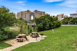 A courtyard with picnic tables, a small bridge, and a large building in the background. - Recently Updated! Beautiful Marsh & Ocean View Retreat | 4 Min to Beach (North Myrtle Beach)