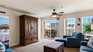 A living room with a large wooden cabinet, a ceiling fan, a blue sofa, and a wicker chest. - Recently Updated! Beautiful Marsh & Ocean View Retreat | 4 Min to Beach (North Myrtle Beach)