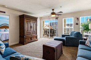 Un salon avec une grande armoire en bois, un ventilateur de plafond et une vue sur l’extérieur, visible à travers une porte-fenêtre coulissante.