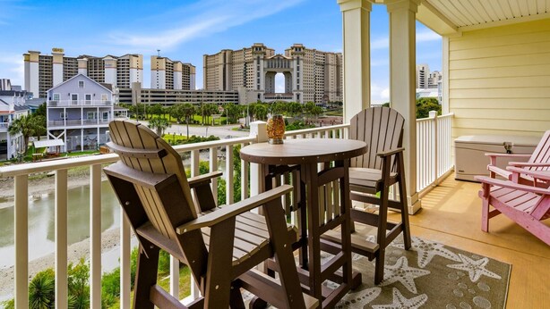 A balcony with wooden chairs, a small table, and a view of high-rise buildings. - Recently Updated! Beautiful Marsh & Ocean View Retreat | 4 Min to Beach (North Myrtle Beach)