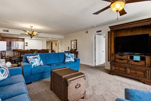 Una sala de estar con un sofá azul, un cofre de mimbre, un mueble de madera para entretenimiento y un ventilador de techo.
