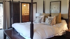 Ein Schlafzimmer mit einem Himmelbett, einer hölzernen Bank, einem Deckenventilator und Wanddekoration.