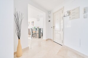 Een hal met een modern interieur, een eetgedeelte op de achtergrond en een witte deur met telefoon en intercom.