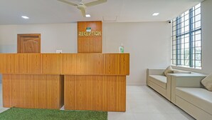 A reception desk with a wooden finish, a ceiling fan, a window with blinds, and a sofa in the background.