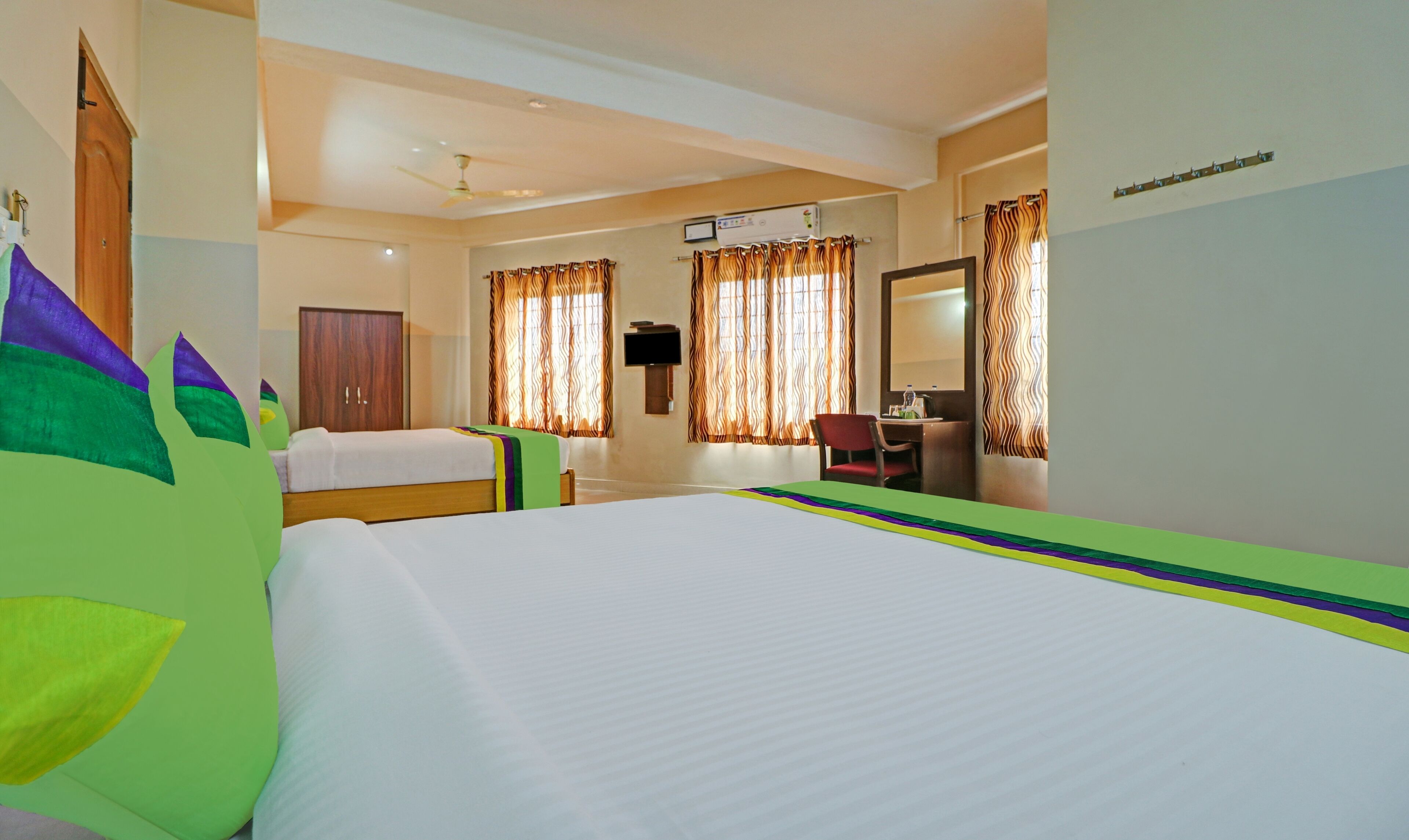 Habitación de hotel con dos camas individuales, un escritorio con silla, un espejo y un televisor en la pared.