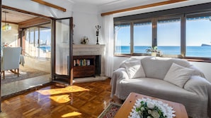 A living room with a sofa, a fireplace, a bookshelf, and a view of the sea.