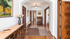 A hallway with a wooden bench, a vase with flowers, a painting, and a door with a decorative handle.